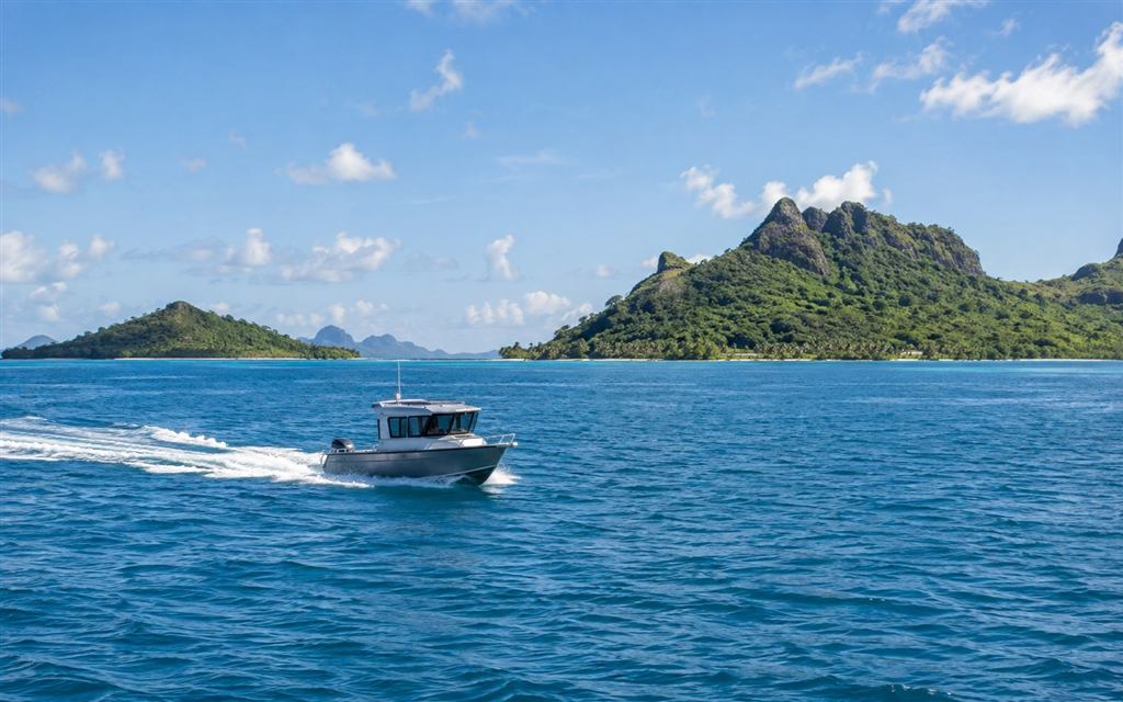A small aluminium cabin boat cruising across blue water by green islands