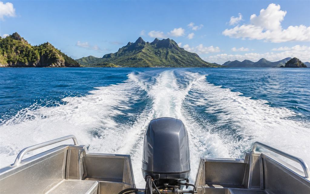 A boat wake crossing blue water toward green tropical islands