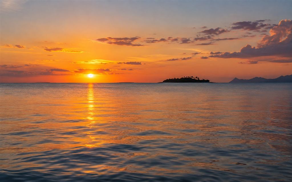 Soft sunset light reflected across calm water and distant islands