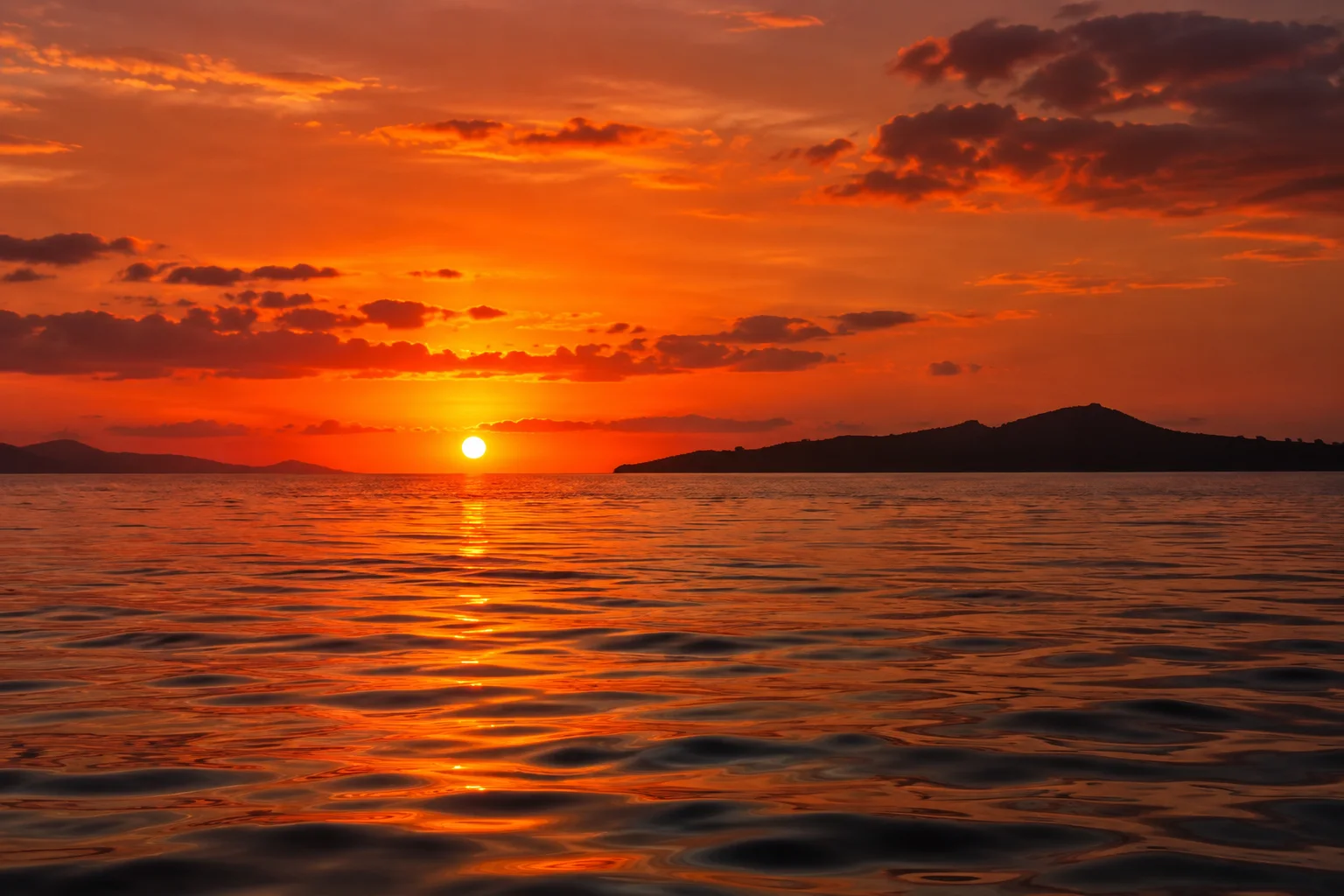 Vivid orange sunset reflected across calm water with a distant island silhouette